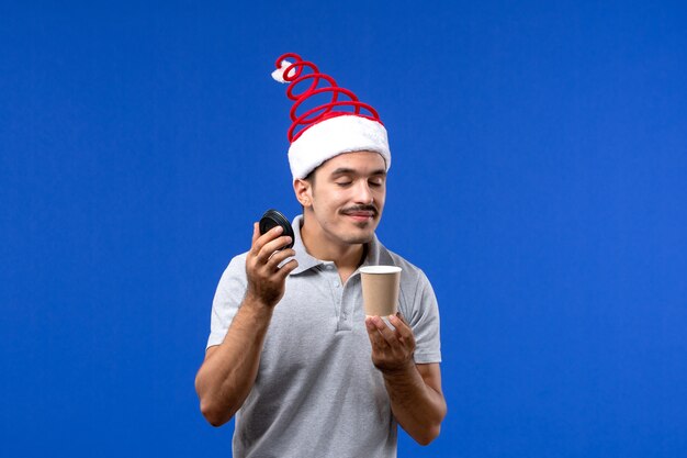 Vista frontal macho joven oliendo café en la pared azul año nuevo emoción de vacaciones masculinas