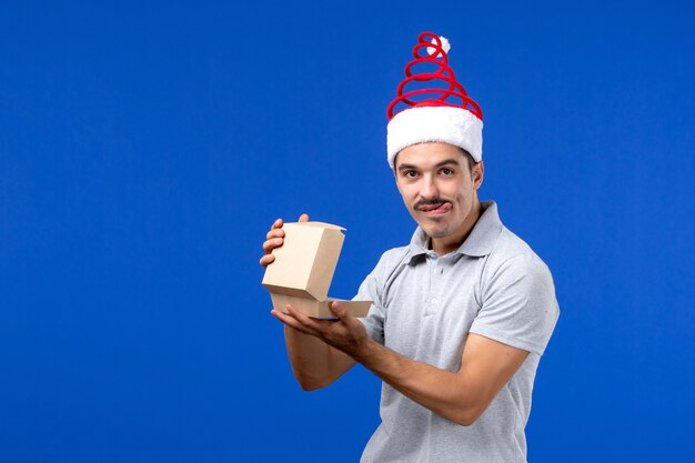 Vista frontal macho joven con paquete de comida en la pared azul trabajo masculino humano servicio de alimentos