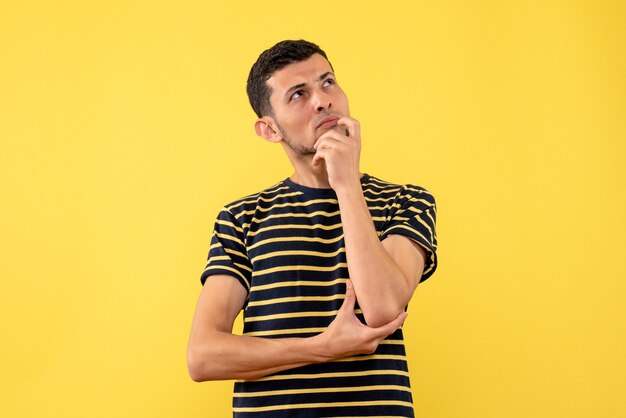 Vista frontal macho joven pensativo en blanco y negro camiseta a rayas fondo amarillo aislado