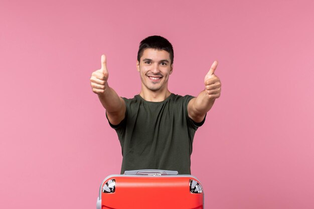 Vista frontal macho joven preparándose para vacaciones sonriendo en espacio rosa