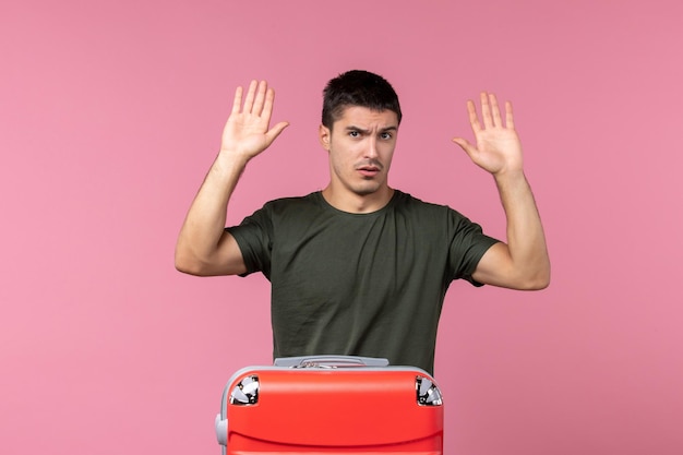 Vista frontal macho joven preparándose para viaje con bolsa roja en espacio rosa