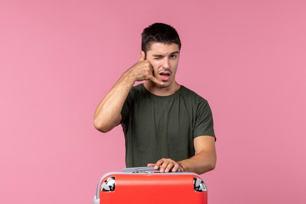 Vista frontal macho joven preparándose para viaje con bolsa roja en espacio rosa