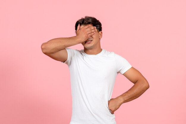 Vista frontal macho joven que cubre la cara en camiseta blanca sobre fondo rosa emoción modelo de color masculino