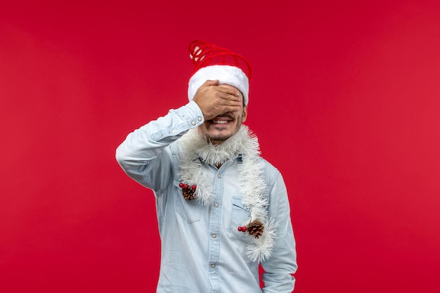 Vista frontal macho joven que cubre sus ojos, vacaciones de navidad rojo