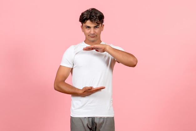 Vista frontal macho joven que muestra el tamaño en camiseta blanca sobre fondo rosa