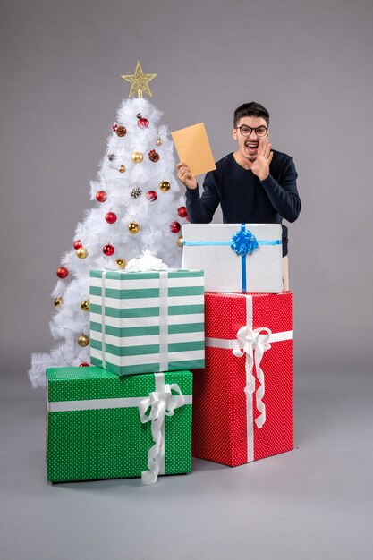 Vista frontal macho joven con regalos y envolver en el gris