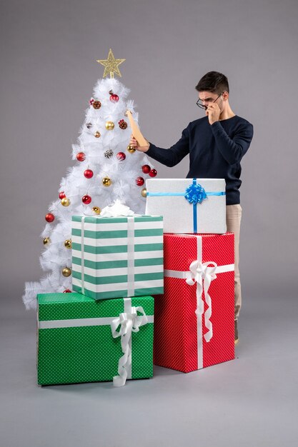 Vista frontal macho joven con regalos y envolver en piso gris año nuevo humano de navidad