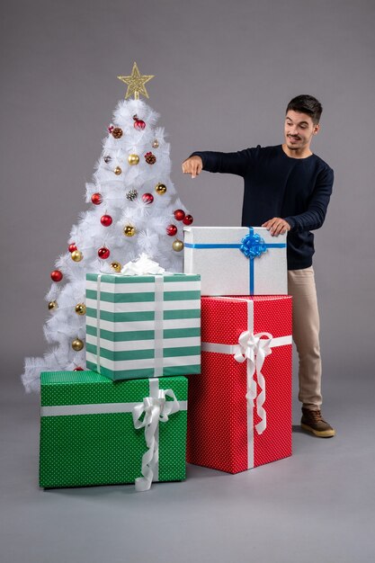 Vista frontal macho joven con regalos de Navidad en gris