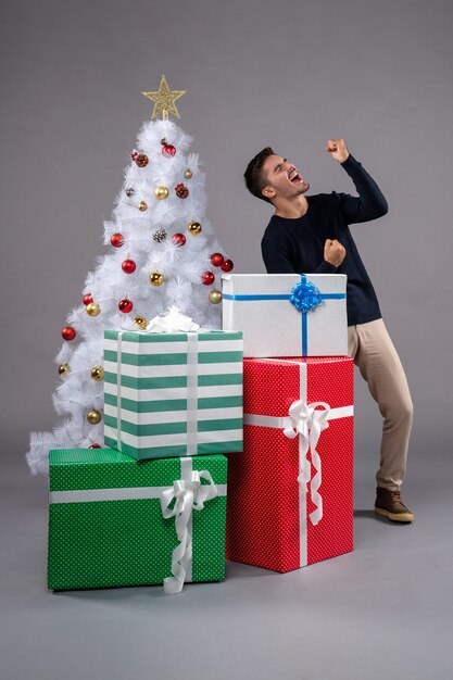 Vista frontal macho joven con regalos de Navidad en gris