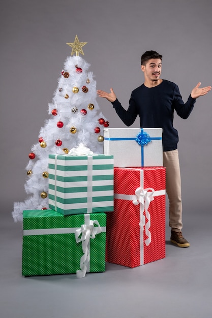 Vista frontal macho joven con regalos de Navidad en gris