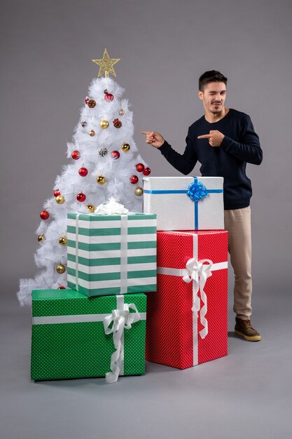 Vista frontal macho joven con regalos de Navidad en gris