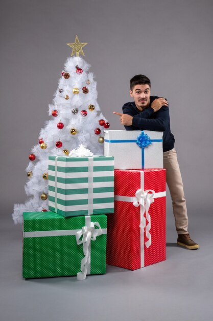 Vista frontal macho joven con regalos de navidad en el piso gris emoción regalo de navidad de año nuevo