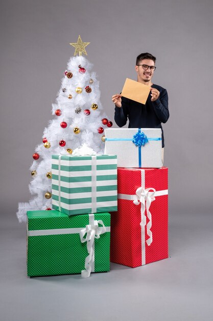 Vista frontal macho joven con regalos navideños en piso gris regalo de navidad humano año nuevo