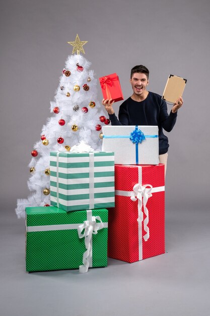 Vista frontal macho joven con regalos de vacaciones en el gris