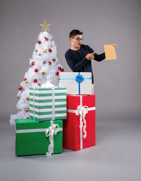 Vista frontal macho joven con regalos de vacaciones en el gris