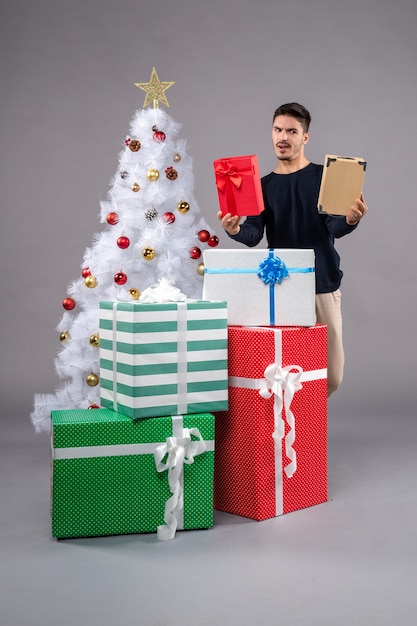 Vista frontal macho joven con regalos de vacaciones en el gris