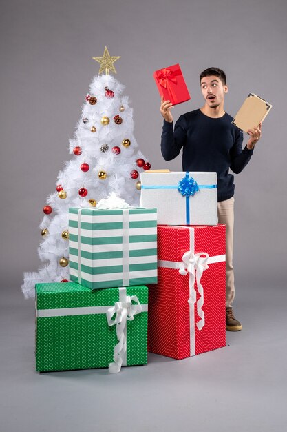 Vista frontal macho joven con regalos de vacaciones en el gris