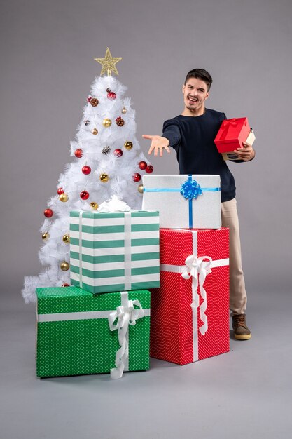 Vista frontal macho joven con regalos de vacaciones en el gris