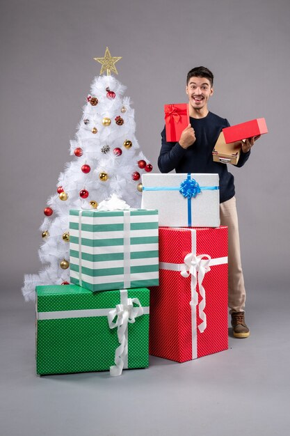 Vista frontal macho joven con regalos de vacaciones en el gris