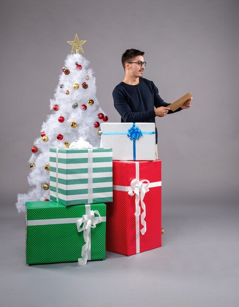 Vista frontal macho joven con regalos de vacaciones en el gris