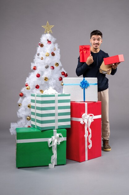 Vista frontal macho joven con regalos de vacaciones en el gris