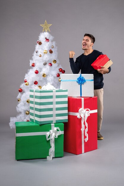 Vista frontal macho joven con regalos de vacaciones en el gris