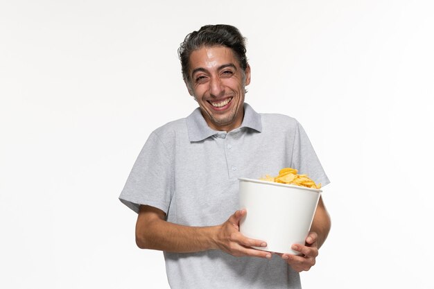 Vista frontal macho joven riendo y comiendo patatas cips en la pared blanca masculina cine de película remota solitario
