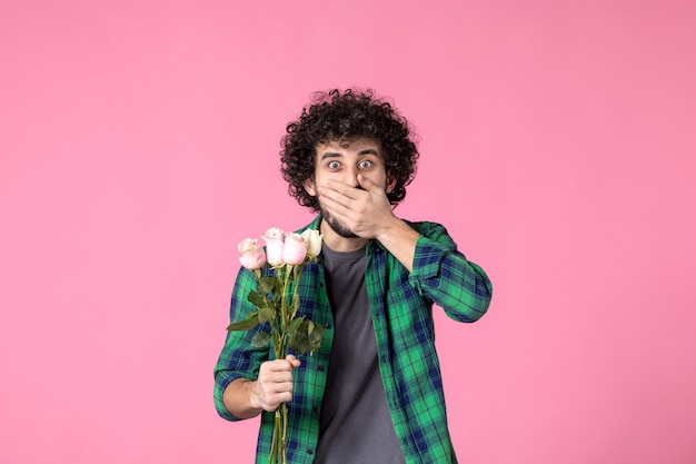 Vista frontal macho joven con rosas rosadas como presente para el día de la mujer en color rosa