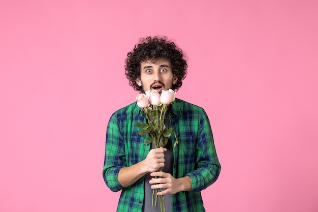 Vista frontal macho joven con rosas rosadas como presente para el día de la mujer en color rosa