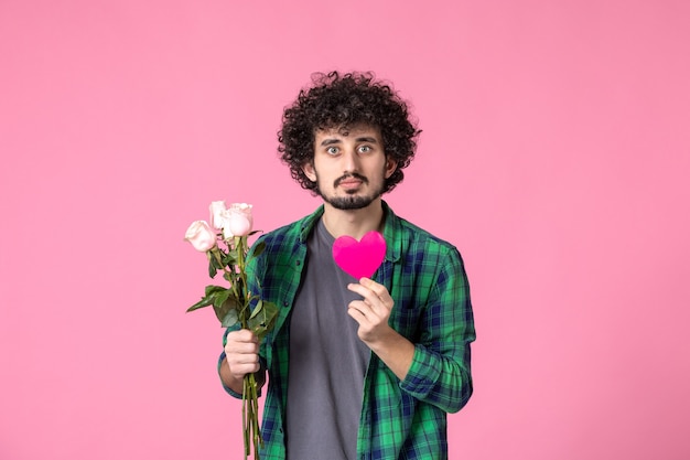 Vista frontal macho joven con rosas rosadas y pegatina de corazón en rosa