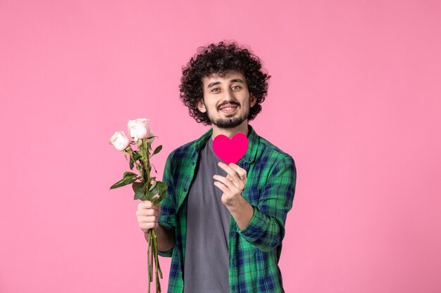 Vista frontal macho joven con rosas rosadas y pegatina de corazón en rosa