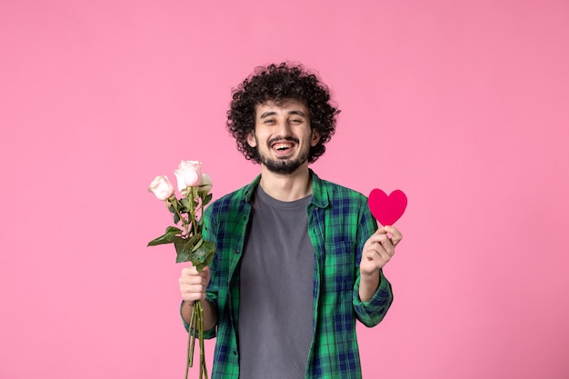 Vista frontal macho joven con rosas rosadas y pegatina de corazón en rosa