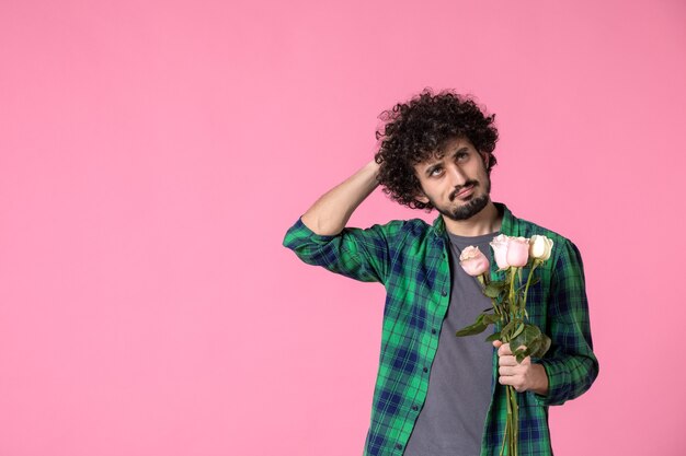 Vista frontal macho joven con rosas rosadas en rosa