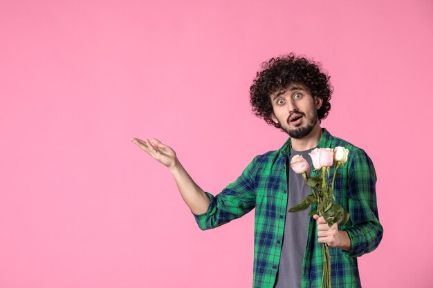 Vista frontal macho joven con rosas rosadas en rosa