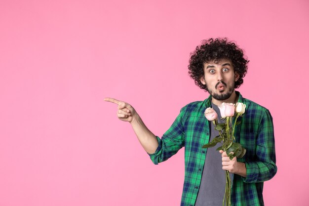 Vista frontal macho joven con rosas rosadas en rosa