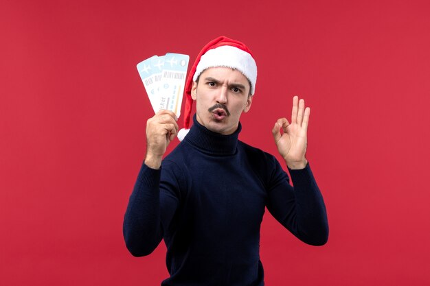 Vista frontal macho joven sosteniendo billetes de avión en el mostrador rojo