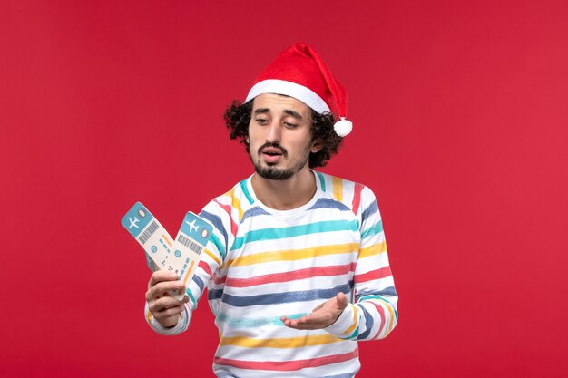 Vista frontal macho joven sosteniendo billetes de avión en la pared roja vacaciones rojas avión de año nuevo