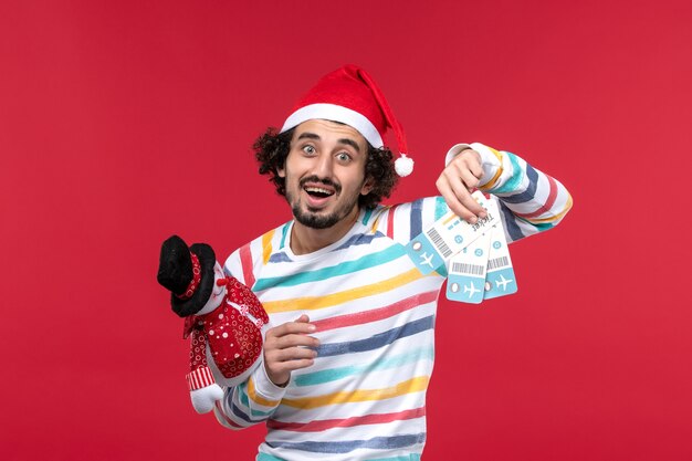 Vista frontal macho joven sosteniendo boletos y juguete en la pared roja macho rojo vacaciones año nuevo