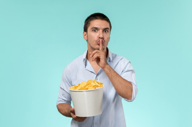 Vista frontal macho joven sosteniendo una canasta con papas fritas y pidiendo estar en silencio sobre una superficie azul