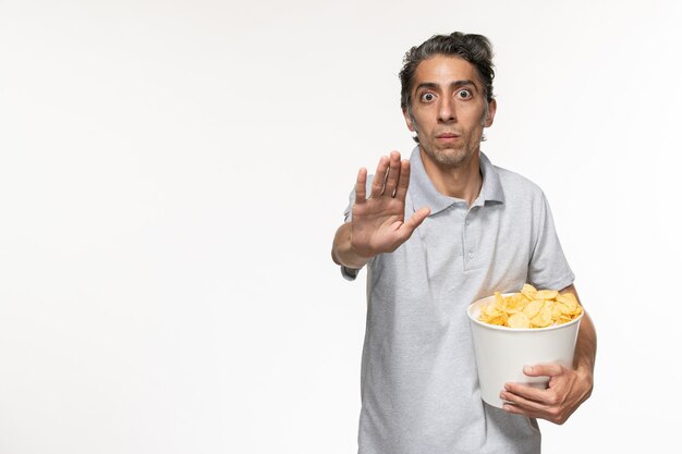 Vista frontal macho joven sosteniendo una cesta con papas fritas y pidiendo que se detenga en una superficie blanca