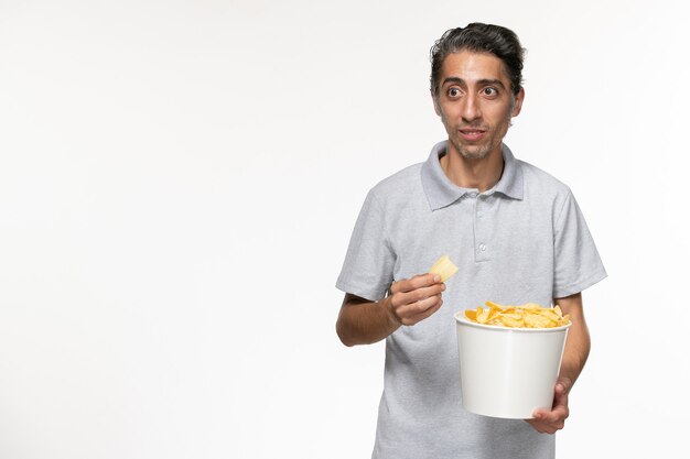 Vista frontal macho joven sosteniendo la cesta con papas fritas en la superficie blanca