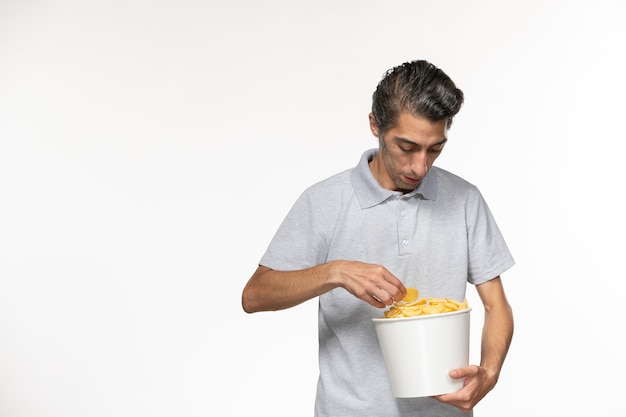 Vista frontal macho joven sosteniendo la cesta con papas fritas en la superficie blanca