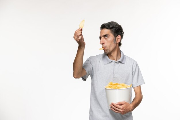 Vista frontal macho joven sosteniendo la cesta con papas fritas en la superficie blanca