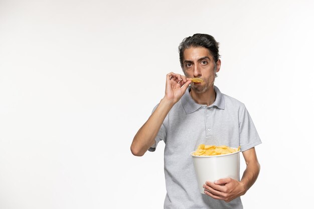 Vista frontal macho joven sosteniendo la cesta con papas fritas en la superficie blanca