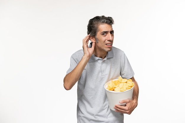 Vista frontal macho joven sosteniendo la cesta con papas fritas y tratando de escuchar sobre una superficie blanca