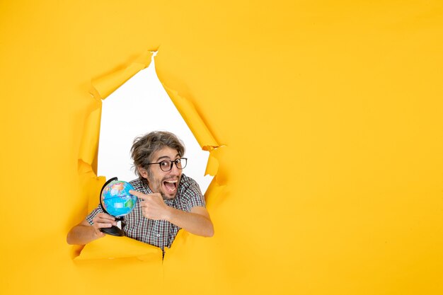Foto gratuita vista frontal macho joven sosteniendo globo terráqueo sobre fondo amarillo emociones del país del mundo vacaciones de planeta de color de navidad