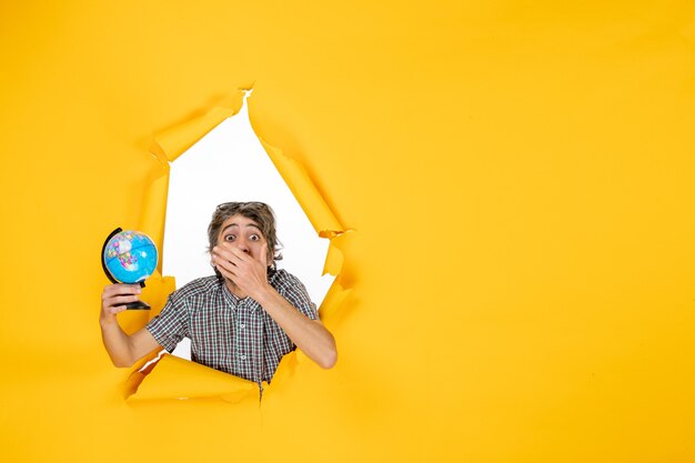 Vista frontal macho joven sosteniendo globo terráqueo sobre fondo amarillo vacaciones emoción navidad país mundo color planeta