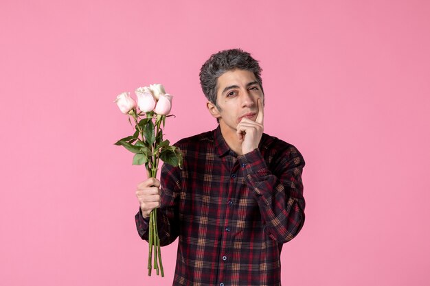 Vista frontal macho joven sosteniendo hermosas rosas rosadas en la pared rosada