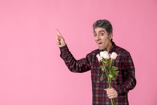 Vista frontal macho joven sosteniendo hermosas rosas rosadas en la pared rosada