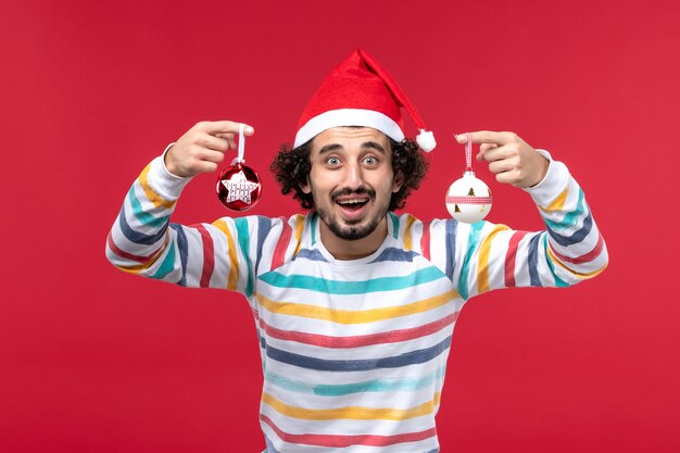 Vista frontal macho joven sosteniendo el juguete del árbol de navidad en una pared roja vacaciones de año nuevo rojo